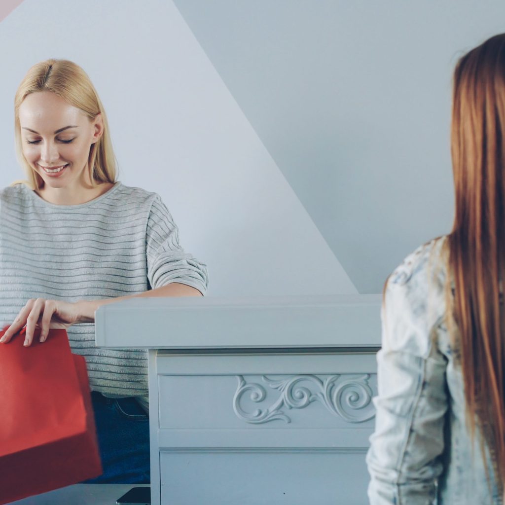 pexels photo 36730431 36730431 Confident cashier handling a colorful red shopping bag for customers in a vibrant store.